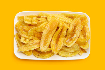 Banana slice chips in white plate on yellow background