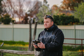 Fototapeta premium Man flying drone holding remote control on country property at sunset