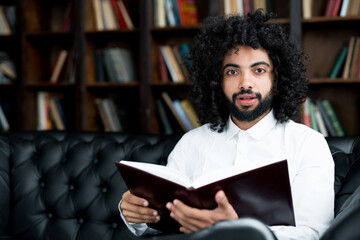 Serious handsome egyptian student preparing for lecture in library holding book