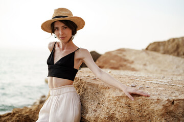 Portrait of woman in black bralette and white trousers leaning on rock at beach