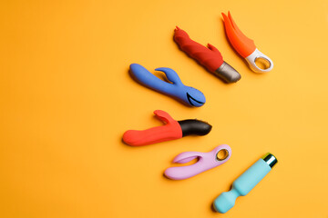Four multi-colored dildos and a vibrator on a yellow background. Clitoral massager, sex toys