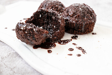 Chocolate muffins on a white plate. Sprinkled with chocolate and coconut on top. Homemade fluffy and juicy chocolate cakes. On a gray background