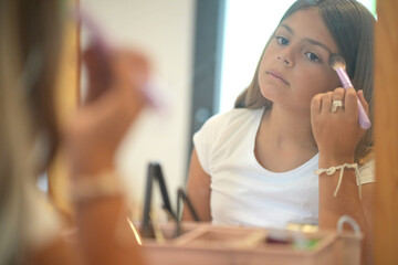 young girl applying makeup in front of a mirror
