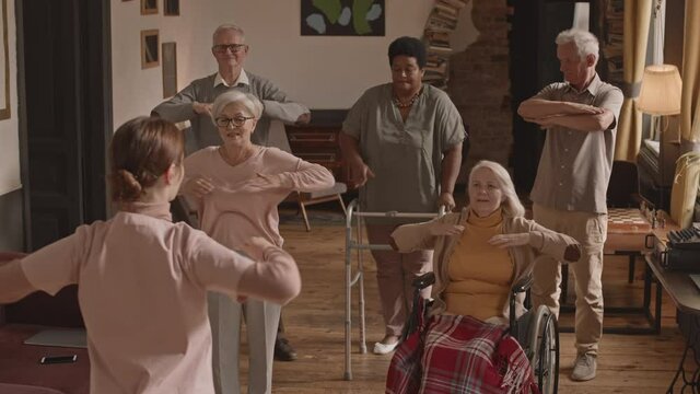 Slowmo shot of group of active multi-ethnic seniors doing physical exercises repeating after nurse in nursing home