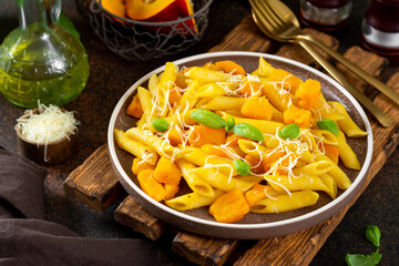 Neapolitan pasta penne rigate with pumpkin in a ceramic plate on a dark culinary background close-up. Traditional Italian cuisine