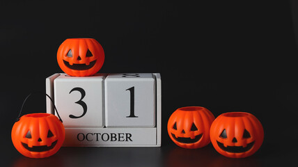 Front view of wooden calendar 31 October with plastic Halloween pumpkins  on black background. Halloween holiday or Halloween party concept