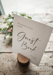 Please sign our guestbook sign at wedding celebration held standing up in wooden stand.  Flowers...