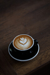 Black cup of coffee latte on wooden table.