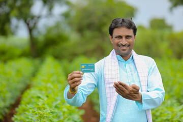 Young indian farmer showing debit or credit card at his green agriculture field