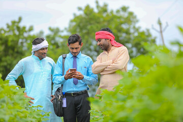 Young indian agronomist or banker showing some information to farmer in smartphone at agriculture field.