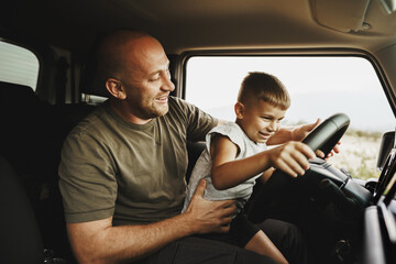 Father teaches little son to drive on road trip