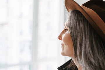 Grey senior woman posing in hat while smiling indoors