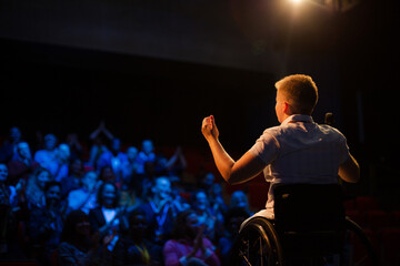 Female speaker in wheelchair on stage waving to audience