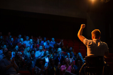 Fototapeta na wymiar Female speaker in wheelchair on stage waving to audience