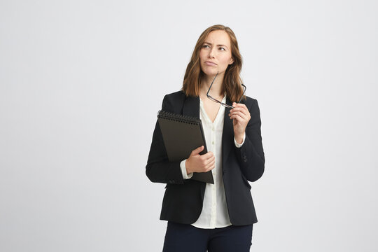 Portrait of a beautiful brunette business woman looking like she's considering something and thinking of it with a computer or laptop or folder in one hand and glasses in the other hand