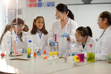Female teacher and students conducting scientific experiment, watching liquid in test tube in laboratory classroom
