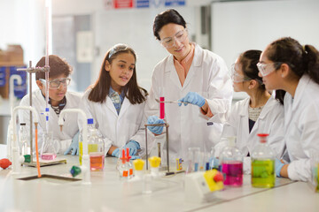 Female teacher and students conducting scientific experiment, watching liquid in test tube in laboratory classroom