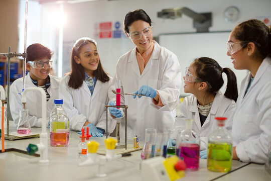 Female teacher and students conducting scientific experiment, watching liquid in test tube in laboratory classroom