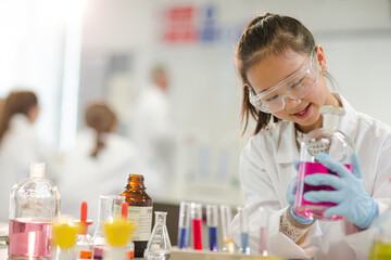 Girl student examining pink liquid, conducting scientific experiment in laboratory classroom