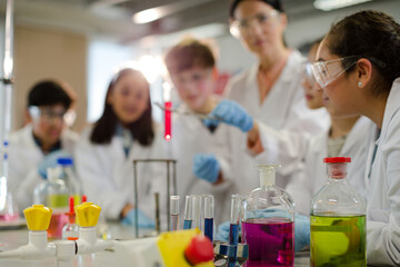 Female teacher and students conducting scientific experiment, watching liquid in test tube in laboratory classroom