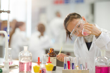 Girl student examining pink liquid, conducting scientific experiment in laboratory classroom