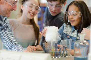 Male teacher and students watching chemical reaction, conducting scientific experiment in laboratory classroom