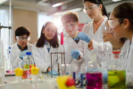Female teacher and students conducting scientific experiment, watching liquid in test tube in laboratory classroom