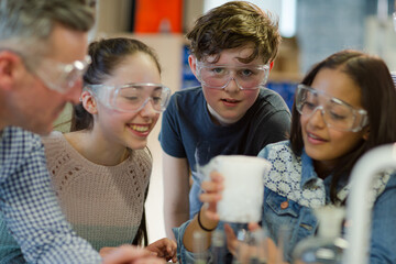 Male teacher and students watching chemical reaction, conducting scientific experiment in laboratory classroom