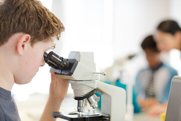 Boy student conducting scientific experiment at microscope and computer in laboratory classroom