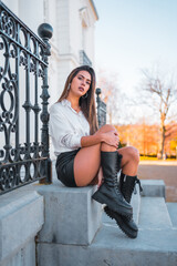 Obraz na płótnie Canvas Lifestyle, fashionable pose of a young brunette in a black leather skirt and shirt smiling on some stairs one autumn afternoon