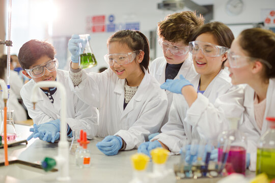 Curious students conducting scientific experiment, examining liquid in beaker in laboratory classroom