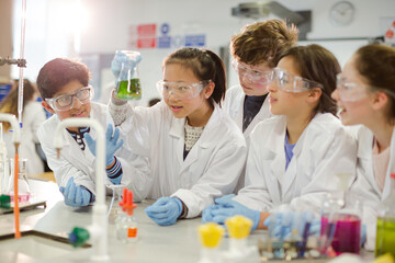 Curious students conducting scientific experiment, examining liquid in beaker in laboratory classroom