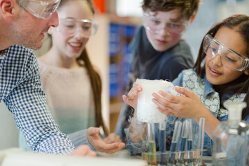 Male teacher and students watching chemical reaction, conducting scientific experiment in laboratory classroom