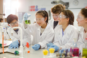 Curious students conducting scientific experiment, examining liquid in beaker in laboratory classroom