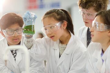 Curious students conducting scientific experiment, examining liquid in beaker in laboratory...
