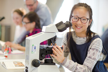 Portrait smiling, confident girl student using microscope, conducting scientific experiment in...