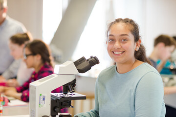 Portrait smiling, confident girl student conducting scientific experiment at microscope in laboratory classroom