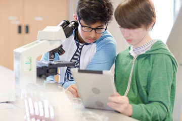 Focused boy students using digital tablet at microscope in laboratory classroom