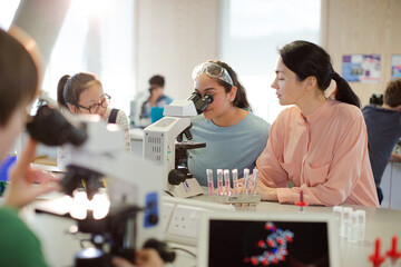 Female teacher and girl student conducting scientific experiment at microscope in laboratory classroom