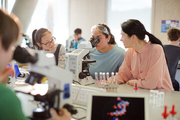 Female teacher and girl student conducting scientific experiment at microscope in laboratory...