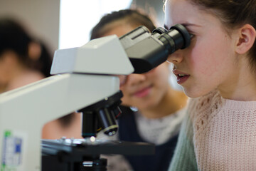 Close up profile girl student using microscope, conducting scientific experiment