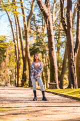 Fototapeta premium Autumn lifestyle, portrait of a young Caucasian brunette girl in a plaid wool sweater and ripped jeans in a park