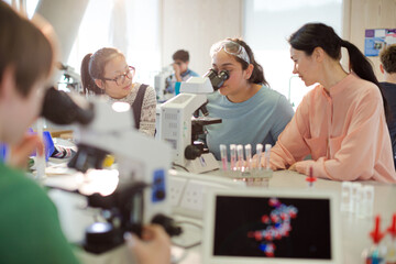 Female teacher and girl student conducting scientific experiment at microscope in laboratory classroom