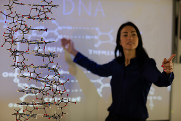 Female science teacher teaching DNA lesson at projection screen