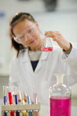 Girl student examining pink liquid, conducting scientific experiment in laboratory classroom