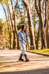 Fototapeta na wymiar Lifestyle, a young Caucasian brunette girl with a plaid wool sweater and ripped jeans walking in a park in autumn
