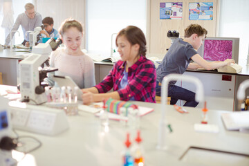 Obraz premium Girl students using microscope, conducting scientific experiment in laboratory classroom