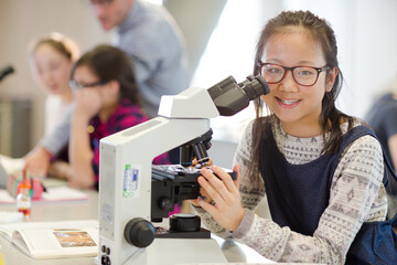 Portrait smiling, confident girl student using microscope, conducting scientific experiment in...