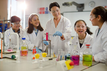 Female teacher and students conducting scientific experiment, watching liquid in test tube in laboratory classroom