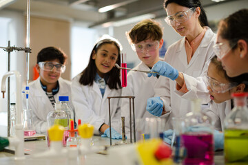 Female teacher and students conducting scientific experiment, watching liquid in test tube in laboratory classroom